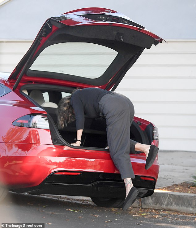 On the street, she pulled over her car and climbed into her trunk, showing off her ankle tattoo