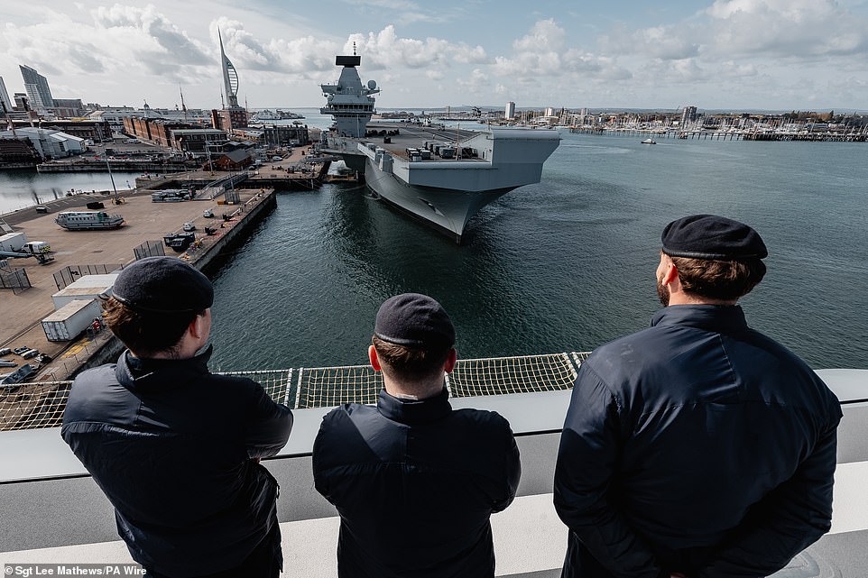 A trio of sailors on HMS Prince of Wales' sister ship, HMS Queen Elizabeth, watch as the aircraft carrier prepares to leave the naval base