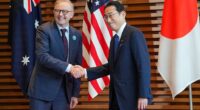 New Australian Prime Minister Anthony Albanese (left) is seeing wearing a bright blue badge to identify him as he shakes hands with Japanese leader Fumio Kishida (right)