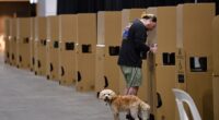 A man is seen casting his vote at an Australian Electoral Commission early voting centre in Melbourne on Monday, May 9, 2022, while his dog looks on