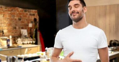 happy full man touching his tummy over kitchen background