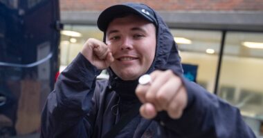 Kneecap rapper poses at surprise performance which Irish trio announced just hours after member was charged with terror offence 'for displaying flag in support of Hezbollah'