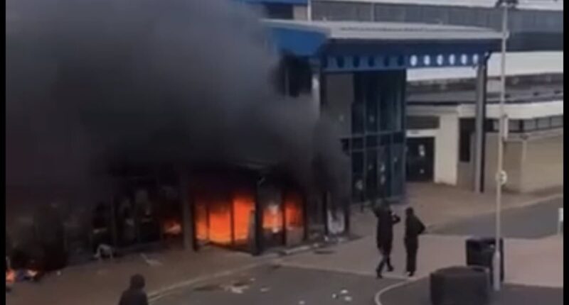 'Anti-migrant' tensions come to a head in Northern Ireland as leisure centre sheltering families who fled Ballymena chaos is set on fire - while riot police battle yobs and terrified locals put up signs showing their nationality